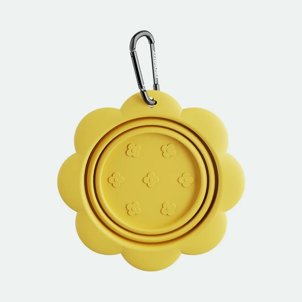 Yellow collapsible bowl folded flat with a carabiner clip through its tab